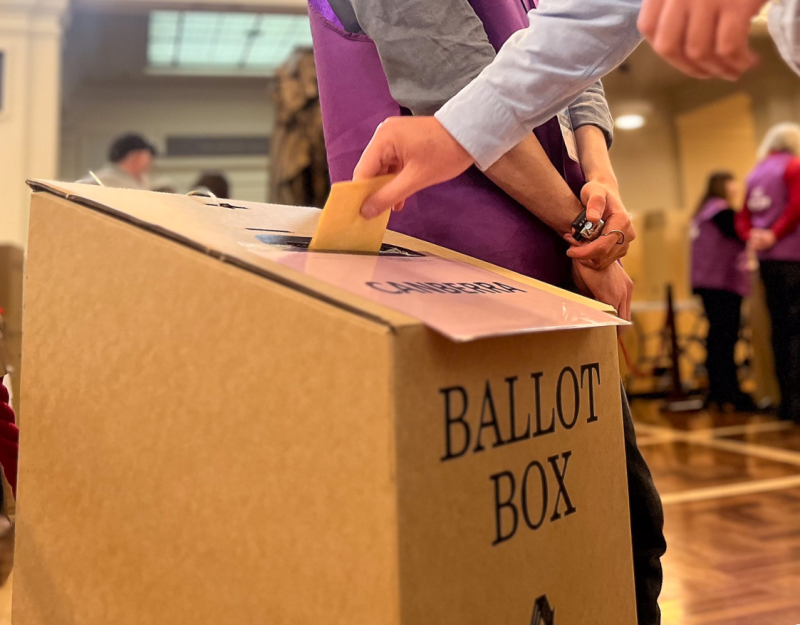 Voter putting a yellow-coloured referendum ballot paper into a cardboard ballot box.