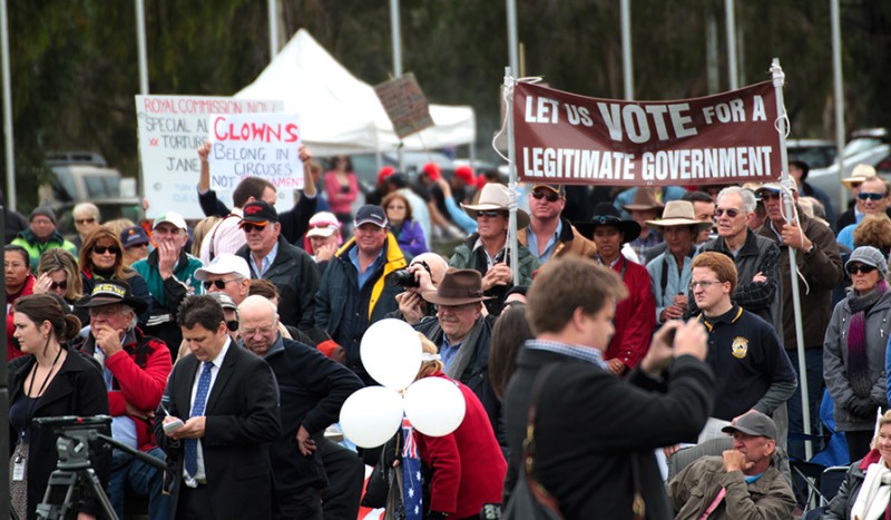 This photo shows a large group of people standing outside with protest signs, such as 'let us vote for a legitimate government'.