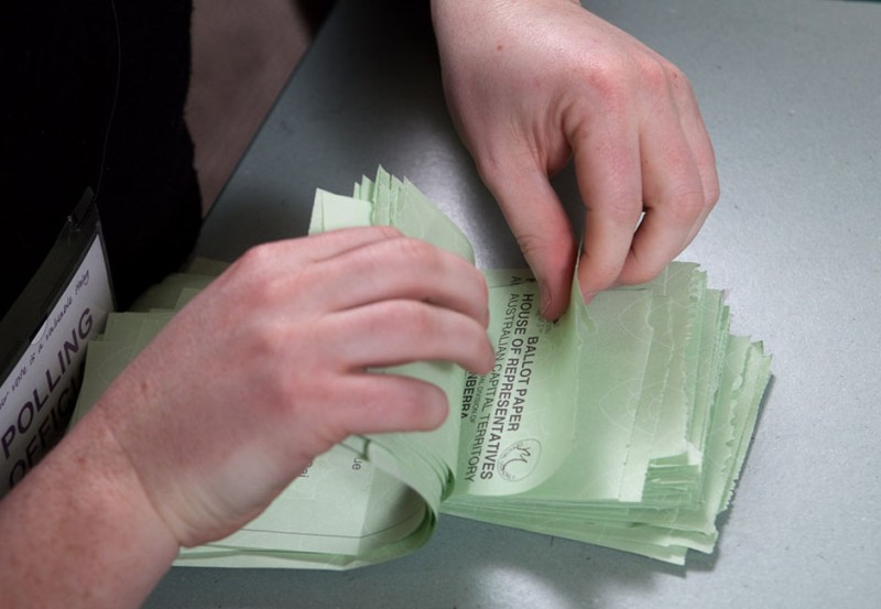 A pair of white hands flick through a pile of light green DL-sized pieces of paper.