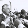 Slide 2: Prime Minister Gough Whitlam surrounded by the press. He is talking into microphones and is surrounded by people.