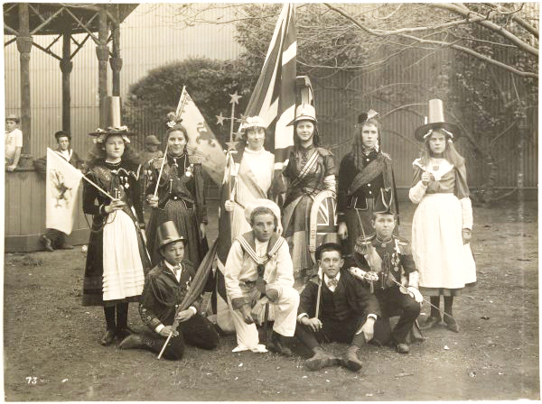 Black and white photo showing 2 rows of children wearing costumes in Melbourne in 1901. They are holding flags and banners.