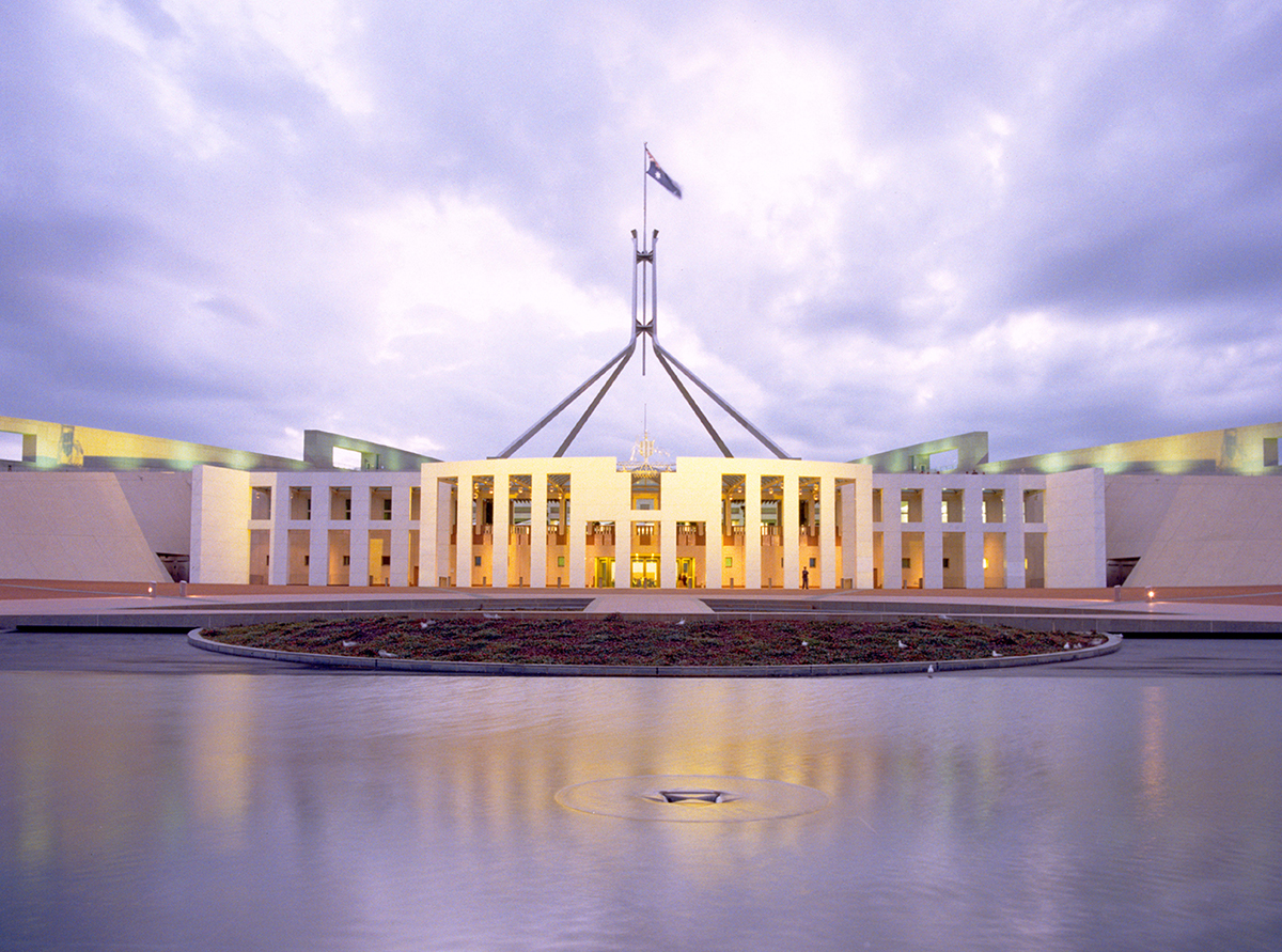 The front of Australian Parliament House with the Great Verandah and the flagmast. In the foreground is water.