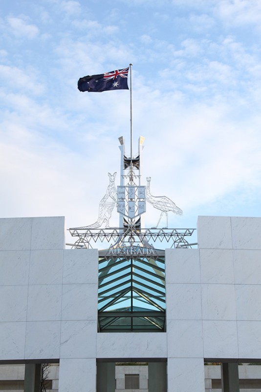 The Commonwealth Commonwealth Coat of Arms and the Australian national flag on top of Australian Parliament House.