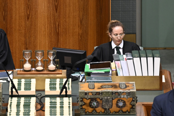 The Deputy Clerk sits at a desk in the House of Representatives. In front of them are large bound books and sand timers.