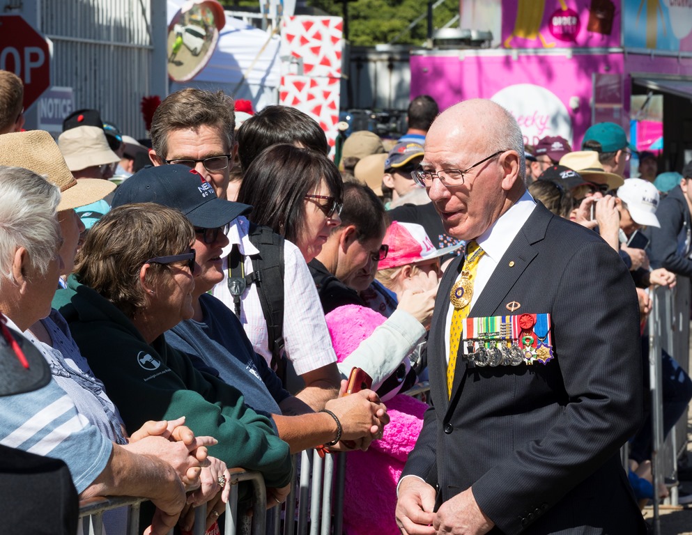 The Governor-General, wearing a suit and medals on the left side of his chest, talks to people in a crowd.