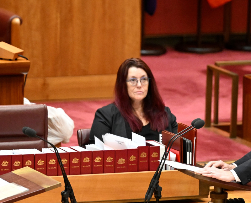 The Deputy Clerk sit a a desk with folders and papers in the Senate.