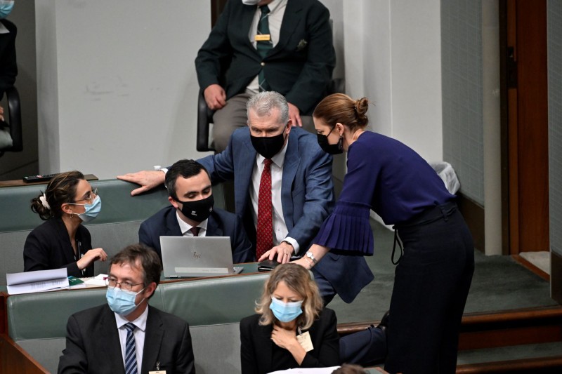 Two members of the House of Representatives lean towards two people sitting down on benches. They are talking and looking at a laptop.