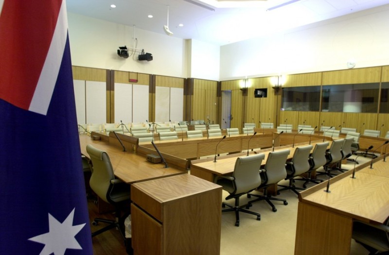 A wood panneled room with 2 rows of wooden desks in a horseshoe shape. An Australian flag is in the foreground.