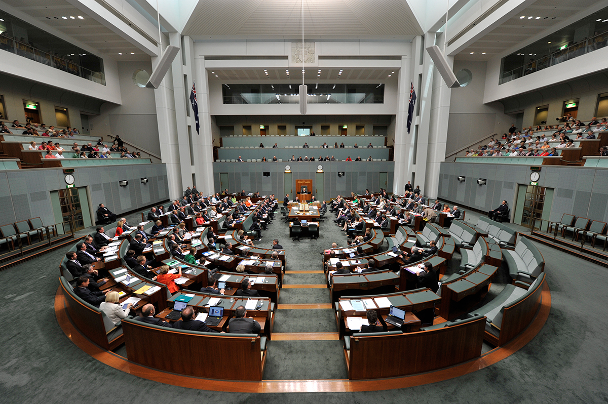 The green House of Representatives. There are people sitting in seats arranged in a U-shape. 