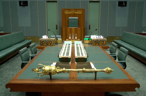 The Mace positioned on brackets on the central table in the green House of Representatives. There are books on the table.
