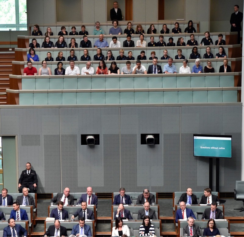 People sitting in rows of benches in a balcony above the House of Representatives.