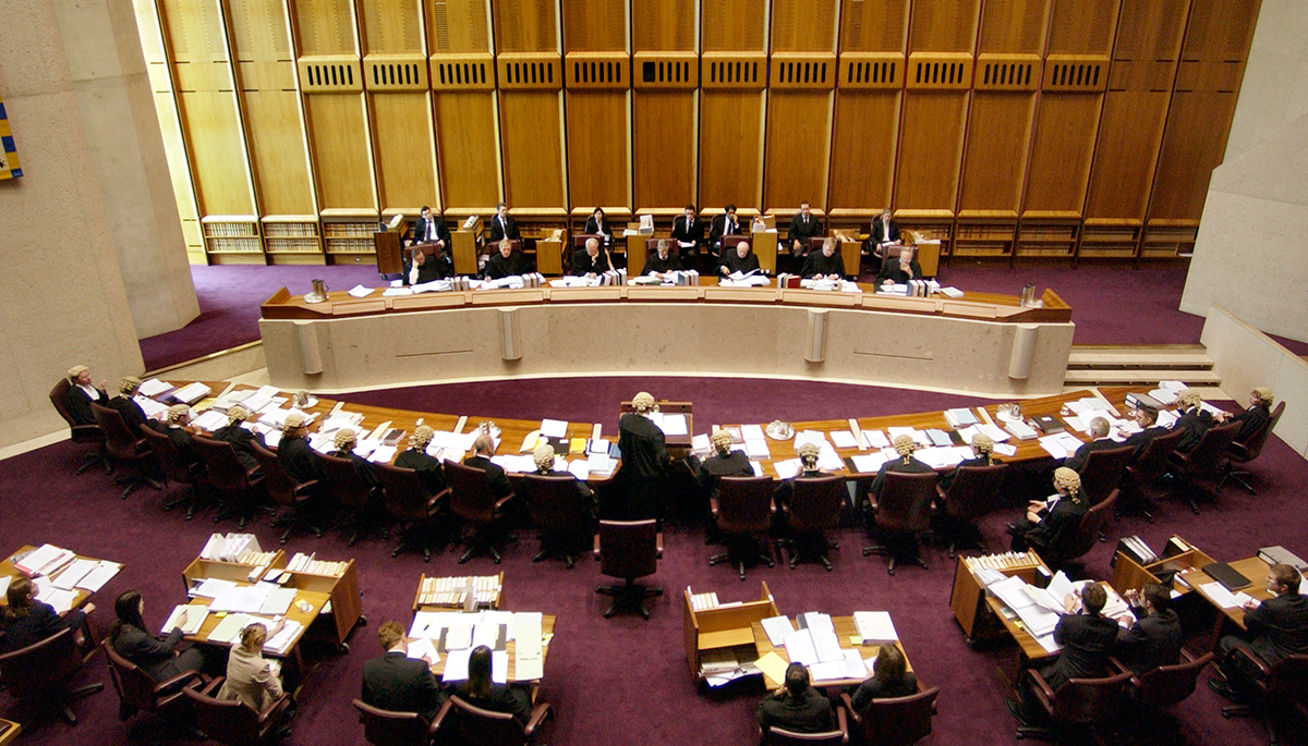 The Australian High Court in session with judges sitting at a long table and lawyers sitting at another table facing them. 