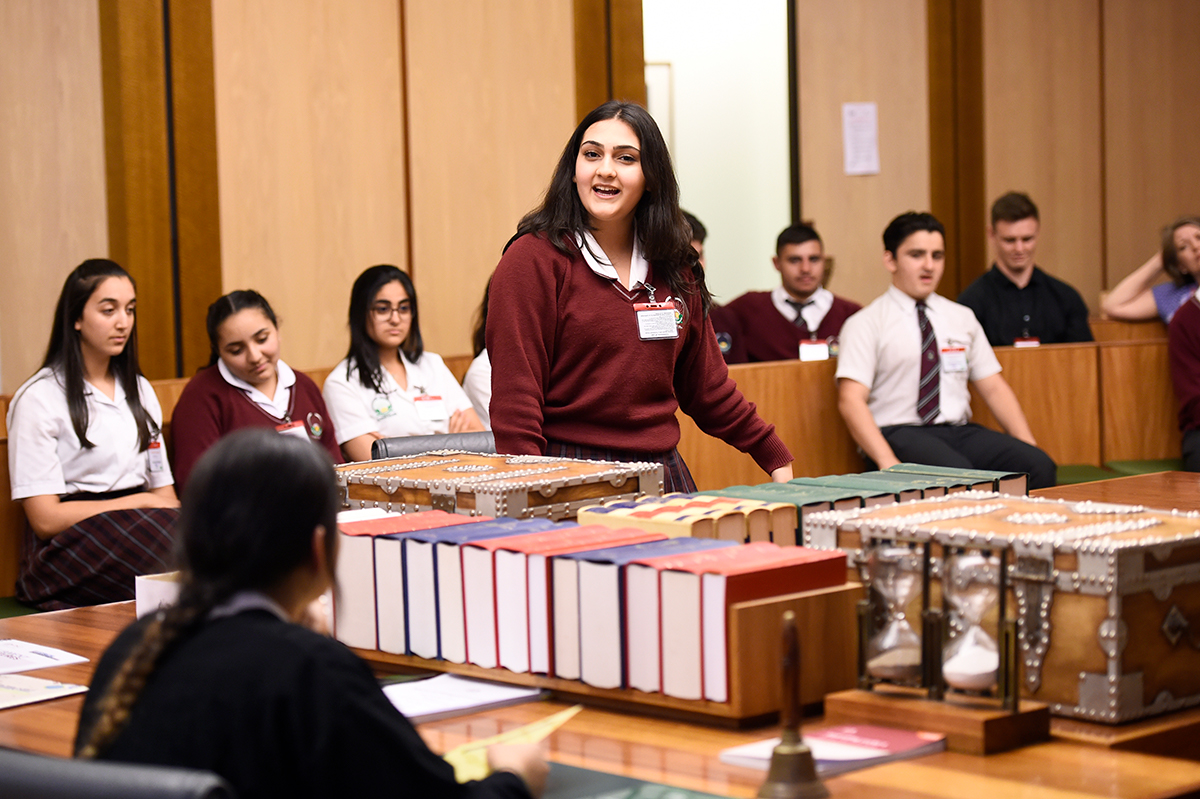 Students in the Education Centre at Parliament House. A student is standing and speaking at a table with boxes and books on it.