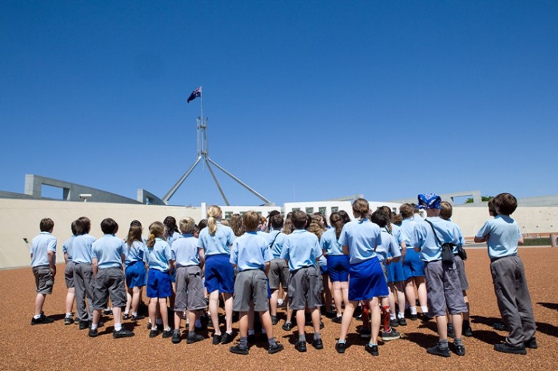 Students on the Forecourt at Australian Parliament House. They are wearing blue uniforms and looking up at the flagmast.